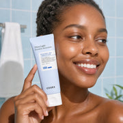 Woman holding COSRX Ultra-Light Invisible Sunscreen beside her cheek