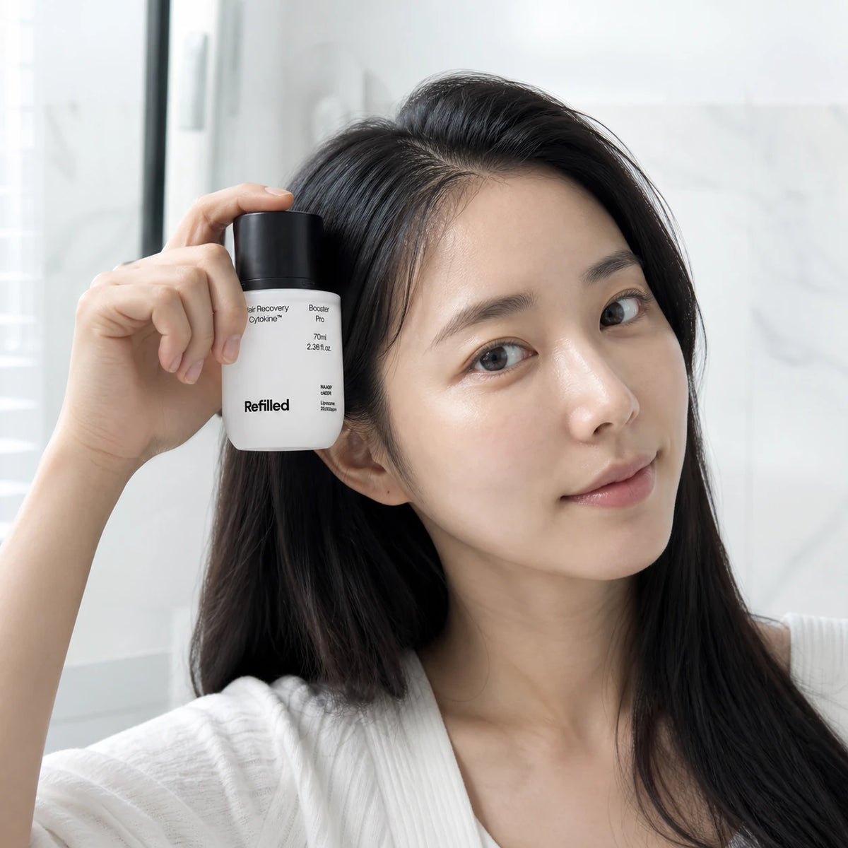 Woman holding Refilled Hair Recovery Cytokine Booster Pro scalp serum near her hair