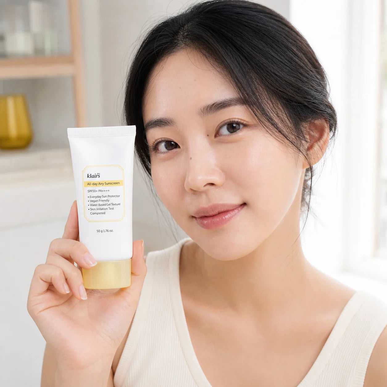 Woman holding Dear, Klairs All-day Airy Sunscreen SPF50+ PA++++ beside her cheek
