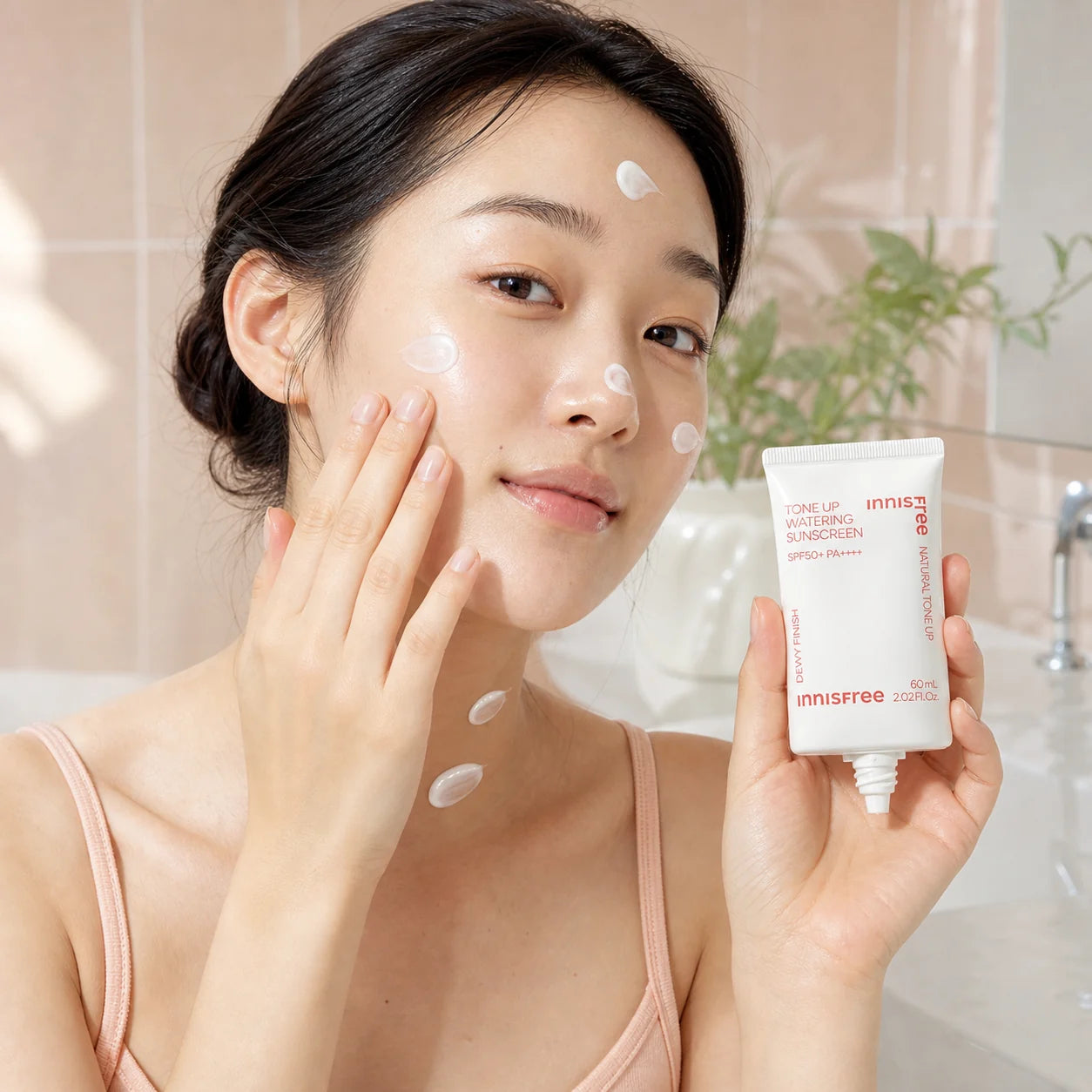 Woman applying Innisfree Tone Up Watering Sunscreen SPF50+ PA++++ to face and neck