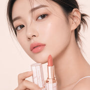 ProtoClinical k-beauty [DEAR DAHLIA] Blooming Edition Lip Paradise Sheer Dew Tinted Lipstick 3.4g angled close-up of a nude pink lipstick bullet with a rosy beige case on a pale background