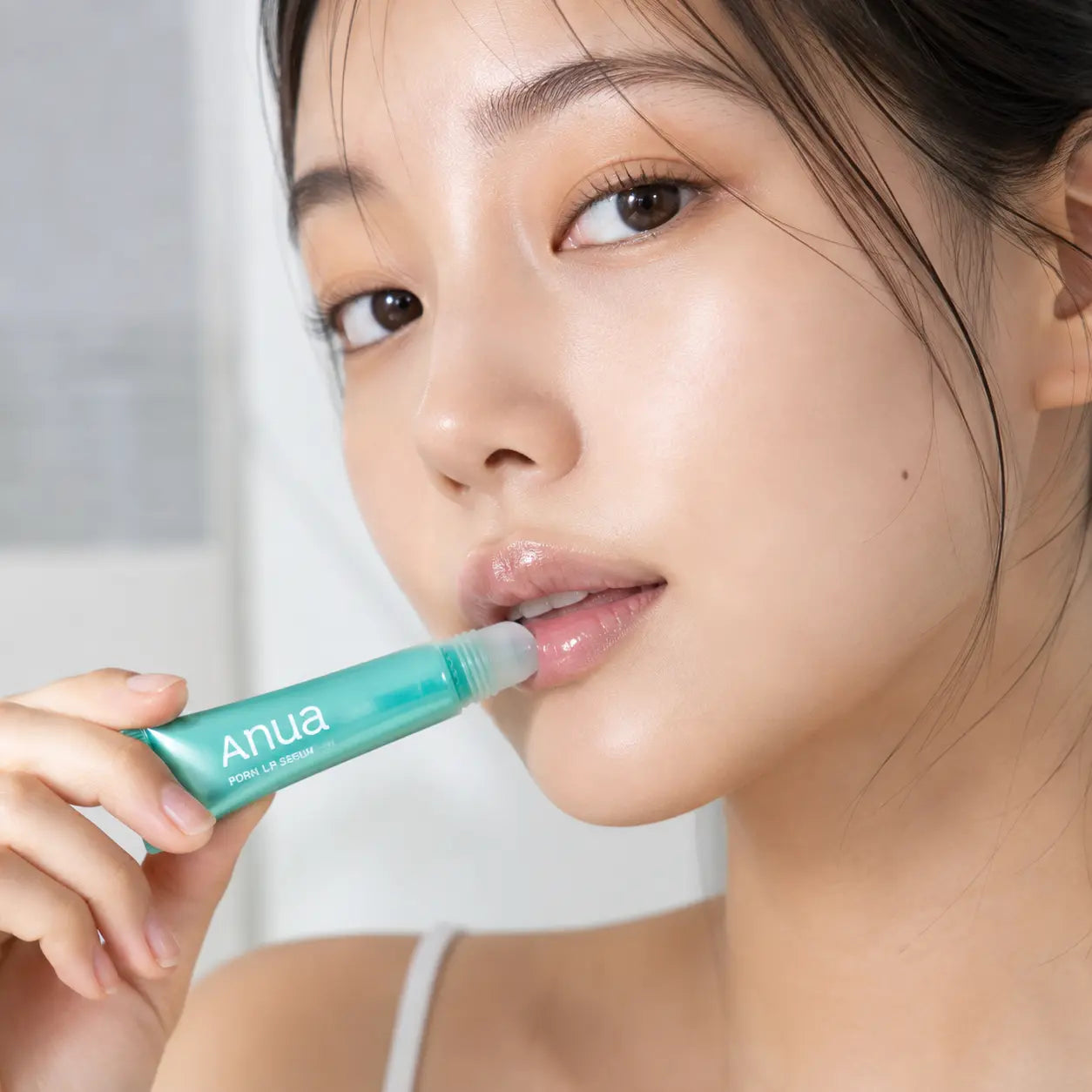 Model applying clear Anua PDRN Lip Serum from its rounded applicator