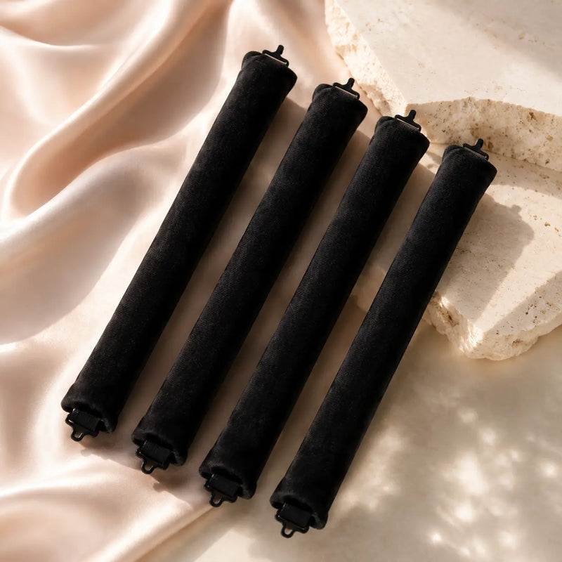Four black velvet heatless curling rods arranged on blush satin and warm ivory stone