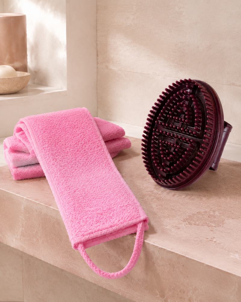 Pink long exfoliating shower towel and burgundy manual brush in the Body Reset Tools kit