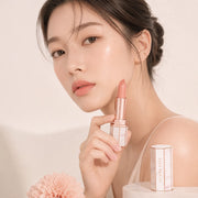 ProtoClinical k-beauty [DEAR DAHLIA] Blooming Edition Lip Paradise Sheer Dew Tinted Lipstick 3.4g close-up of a nude peach lipstick bullet in a slim beige tube on a pale blush background