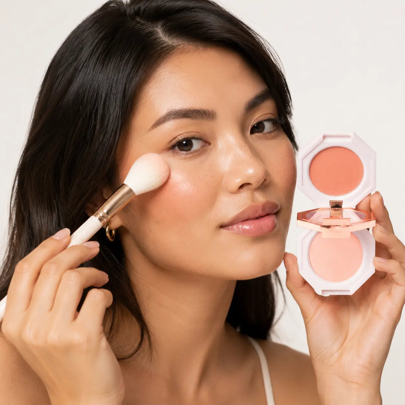 Model applying DEAR DAHLIA Fair Lady coral nude blush while holding the open dual compact