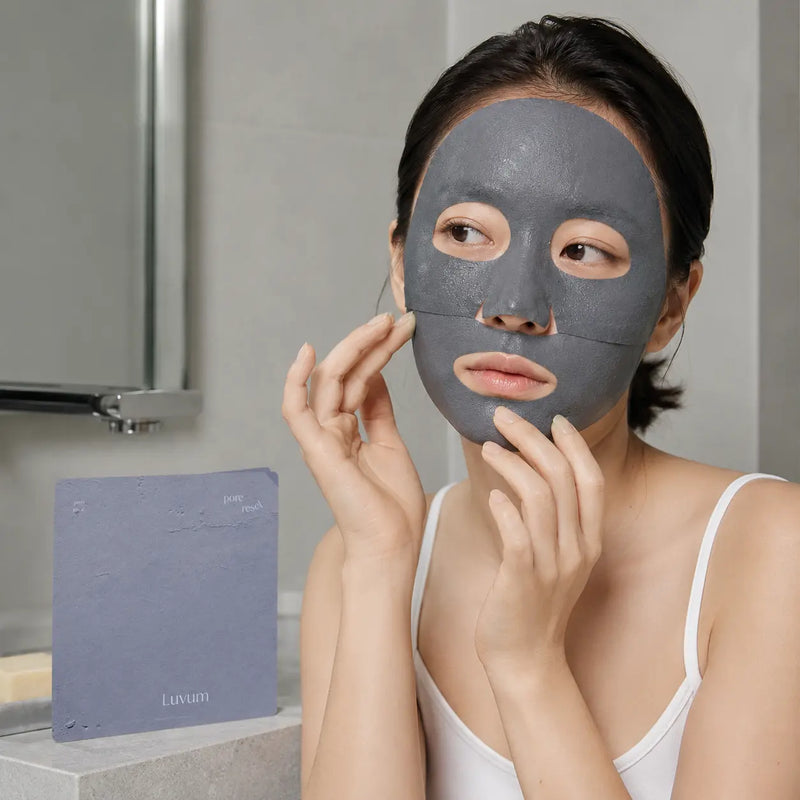 Woman applying the charcoal gray Luvum Pore Reset Mud Sheet Mask