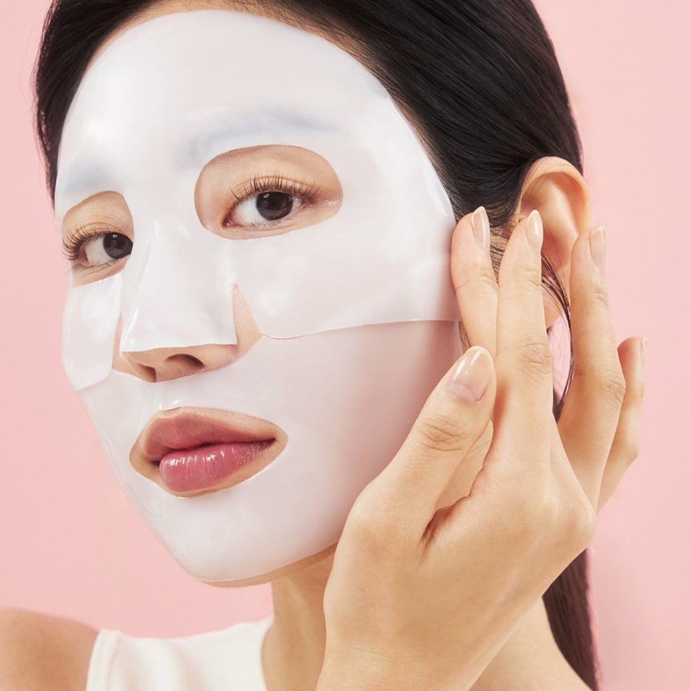 Model applying the white Biodance Bio-Collagen hydrogel mask to her face against a pink background.