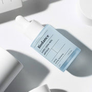 ProtoClinical k-beauty BIODANCE: Hydro Cera-nol Ampoule (30ml) pale blue dropper bottle angled on a white surface with strong shadows and torn paper edges