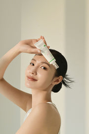 AXIS-Y Complete No-Stress Physical Sunscreen V.3 50ml by ProtoClinical shown in a model-style lifestyle photo with the sunscreen packaging for a k-beauty skincare routine.