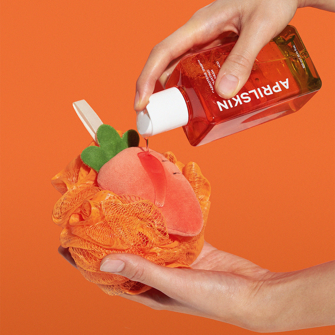 APRILSKIN Carrotene IPMP Exfoliating Body Wash 300ml by ProtoClinical displayed in a thumbnail-style graphic featuring the body wash bottle and shower ball accessory for a k-beauty body care routine.