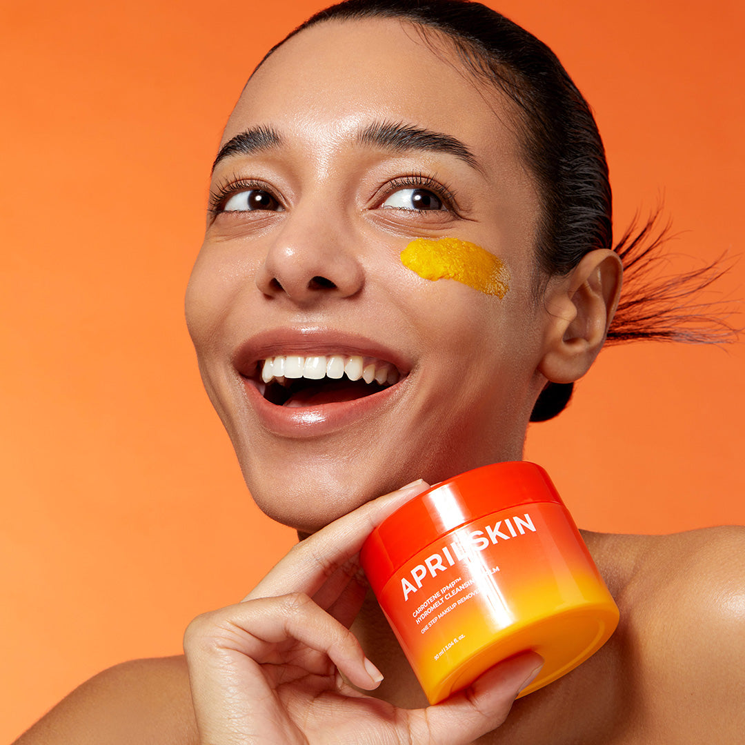 APRILSKIN Carrotene IPMP Hydromelt Cleansing Balm 90ml by ProtoClinical displayed in a promotional skincare visual with the cleansing balm and lifestyle styling for a k-beauty routine.