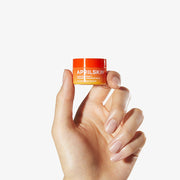 ProtoClinical k-beauty APRILSKIN MINI Carrotene IPMP Hydromelt Cleansing Balm 10ml single orange cleansing balm jar centered on a warm beige background with pale blue side accents.