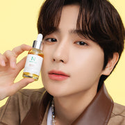 ProtoClinical k-beauty portrait of a person with dark hair wearing a brown top against a pale yellow background.