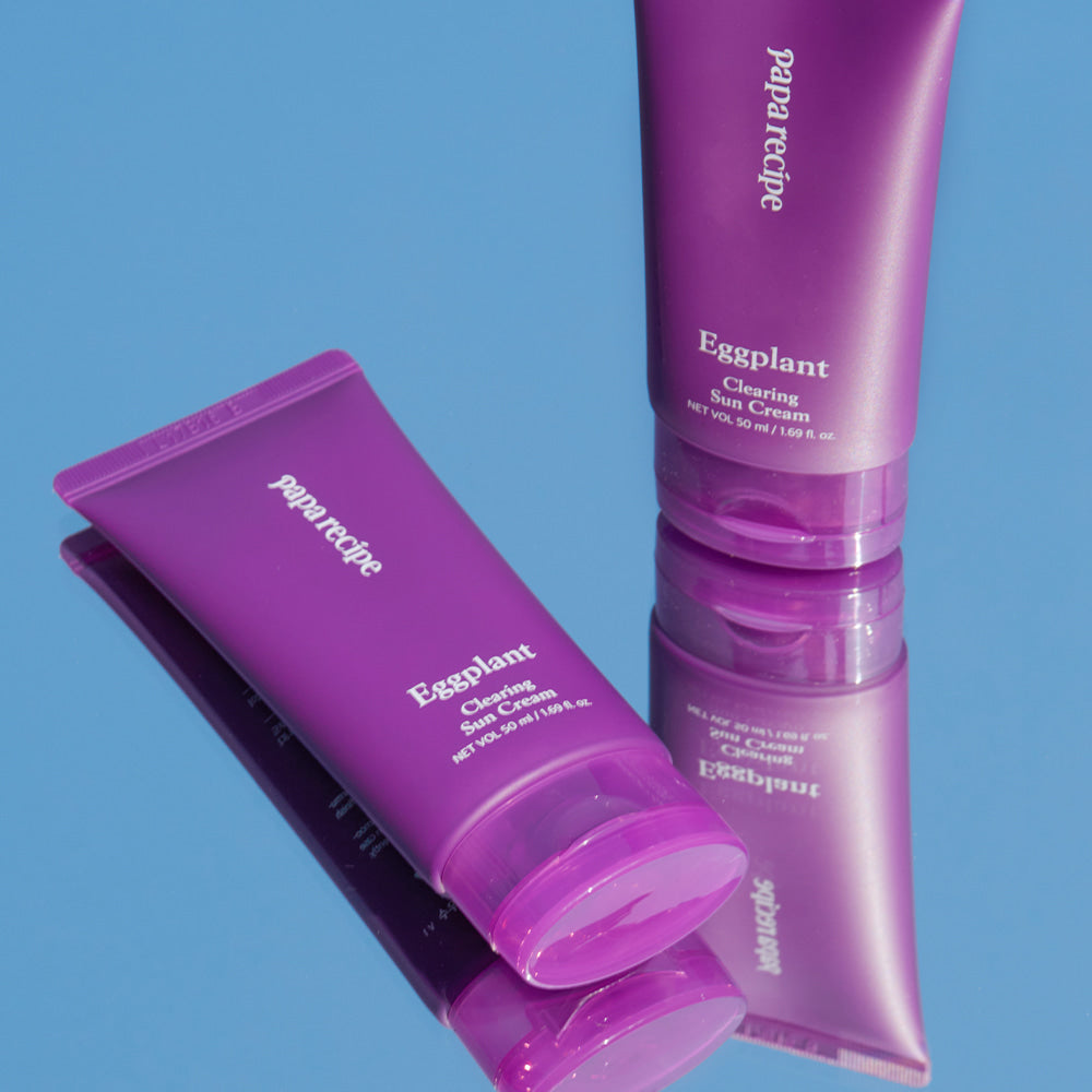 ProtoClinical k-beauty papa recipe Eggplant Clearing Sun Cream 50ml (SPF 50+ PA++++) promotional panel with a close-up of a woman touching her cheek, black Korean text, and a lavender-and-white background