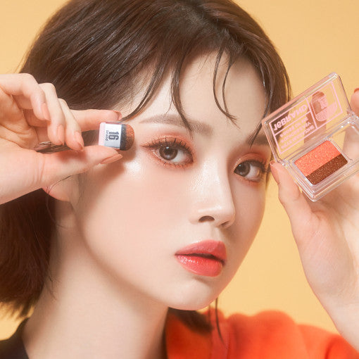 ProtoClinical k-beauty 16BRAND Sixteen Eye Magazine (7colors) close-up of a model holding the dual eyeshadow compact and applicator against a warm peach background