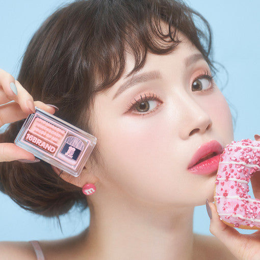 ProtoClinical k-beauty 16BRAND Sixteen Eye Magazine (7colors) close-up of a model holding the pink dual eyeshadow compact beside a frosted pink donut on a pale blue background