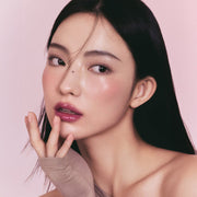 ProtoClinical k-beauty 3CE Sheer Liquid Blusher 3g close-up portrait of a woman with dark hair, warm peach makeup, and a soft beige background