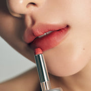 ProtoClinical k-beauty Oddtype Unseen Blur Tint single upright lip tint tube centered on a peach beige background with pale aqua corner accents