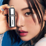 ProtoClinical k-beauty Oddtype Unseen Mirror Tint single upright warm brown lip tint tube centered on a deep taupe background with a soft blue corner accent