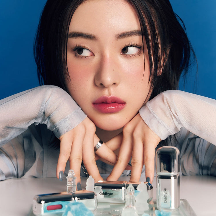 ProtoClinical k-beauty Oddtype Unseen Mirror Tint single upright peach lip tint tube centered on a cool blue background with dark navy side gradients