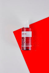 ProtoClinical k-beauty PAUL MEDISON Signature Body Mist 211ml #Baby Powder single translucent pink-red body mist bottle standing upright against an angled red panel with water droplets on a white background
