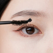 ProtoClinical k-beauty DR.BANGGIWON EYELASH BLACK SERUM 11ml close-up of a brown eye with a black spoolie brush brushing the upper lashes against a skin-toned background