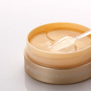 ProtoClinical k-beauty PETITFEE Gold Hydrogel Eye Patch (1.4g X 60 Patches) single warm gold eye patch package laid horizontally on a pale blue and cream background