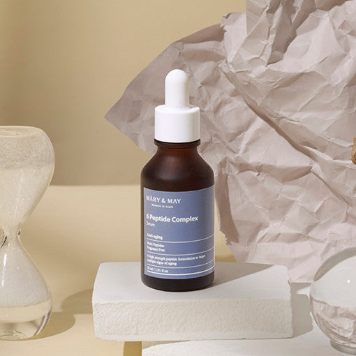 ProtoClinical k-beauty [MARY & MAY] 6 Peptide Complex Serum 30ml as a dark gray vertical serum bottle silhouette centered on a light background with warm beige and muted mauve side panels