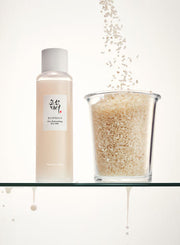 ProtoClinical k-beauty [Beauty of Joseon] Glow Replenishing Rice Milk 150ml pale bottle and matching box side by side on a light background with soft aqua and beige shading