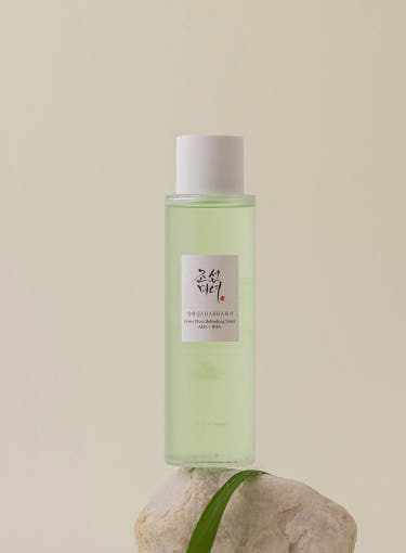 ProtoClinical k-beauty [Beauty of Joseon] Green Plum AHA BHA Toner 150ml translucent light green toner bottle with a white cap standing on a pale stone with a green leaf against a warm beige background
