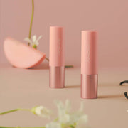 ProtoClinical k-beauty [MACQUEEN New York] Better Than Kiss Lip Balm 3.5g (3-type) two soft pink lip balm tubes standing upright beside peach slices and small flowers on a warm beige background