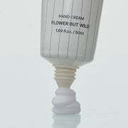 ProtoClinical k-beauty SENNOK Hand Cream Flower But Wild 50ml in a close-up of the white tube dispensing a dollop of cream from the open nozzle onto a pale blue surface