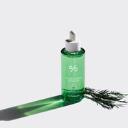 ProtoClinical k-beauty Dr.Ceuracle Tea Tree Purifine 95 Essence 50ml single upright green essence bottle centered above a gray lower band on a pale pastel background