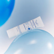 ProtoClinical k-beauty [THE LAB by BLANC DOUX] Oligo Hyaluronic Acid Sun Essence SPF50+ PA++++ 40ml white tube lying diagonally across pale blue balloons on a soft light background