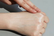 ProtoClinical k-beauty [THE LAB by BLANC DOUX] Oligo Hyaluronic Acid Sun Essence SPF50+ PA++++ 40ml creamy sunscreen swatched across the back of a hand with fingers blending it on a light gray background