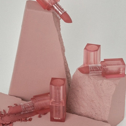 ProtoClinical k-beauty BBIA Last Powder Lipstick 3.5g three rosy nude lipstick tubes arranged on pink geometric blocks with one lipstick open above a powder-textured base