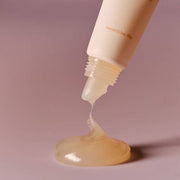 ProtoClinical k-beauty AROMATICA Glow Vita Lip Volumizer Orange & Neroli 10g close-up of the tube nozzle dispensing translucent gloss onto a soft pink surface