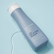 ProtoClinical k-beauty [Daeng Gi Meo Ri] Look At Hair Loss True Hair & Scalp Shampoo 500ml shown as an abstract beauty close-up with a blurred dark vertical form on a pale aqua and blue background.