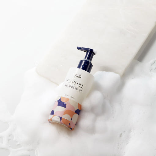ProtoClinical k-beauty Foellie Capsule Feminine Wash 200ml bottle angled in white foam with a navy pump and a peach-patterned lower label