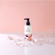 ProtoClinical k-beauty Foellie Capsule Feminine Wash 200ml upright bottle on a glossy white surface with translucent spheres and spilled liquid against a pink background