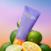 ProtoClinical k-beauty NEOGEN Dermalogy Double Vita Capsule Cleansing Foam 160g in a purple cleanser tube leaning over whole and sliced citrus fruit on a pink to blue gradient background