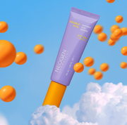 ProtoClinical k-beauty NEOGEN Dermalogy Double Vita Watery Sun Serum 50ml lavender sun serum tube angled above white clouds with floating orange capsules on a bright blue sky background
