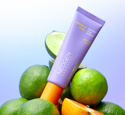 ProtoClinical k-beauty NEOGEN Dermalogy Double Vita Watery Sun Serum 50ml lavender tube leaning over whole and sliced limes with an orange cap on a cool blue gradient background