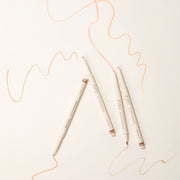 ProtoClinical k-beauty [TOO COOL FOR SCHOOL] Artclass Glam Under Liner 0.2g/0.7g (4 Colors) four cream liner pens arranged diagonally on a light cream background with peach and beige swatch lines