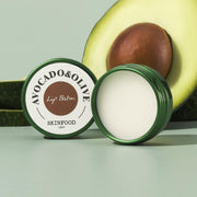 ProtoClinical k-beauty SKINFOOD Avocado & Olive Lip Balm 12g single olive-green lip balm tube standing upright between dark olive side panels on a pale yellow and aqua background
