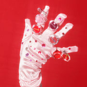 ProtoClinical k-beauty AMUSE Ring Lip Balm 0.9g (5 Colors) shown as five clear ring-pack lip balms posed on a jeweled white satin glove against a vivid red background