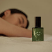 ProtoClinical k-beauty AROMATICA Sleep Tight Pillow Mist 100ml dark spray bottle beside a cream pillow in a warm brown bedroom scene