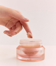ProtoClinical k-beauty HEVEBLUE Chaga Cica Exosome Derma Coating Balm 55g open translucent pink balm jar with a hand dipping a fingertip into the cream on a pale background