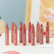 ProtoClinical k-beauty CLIO Butter Balm Crayon + Sharpener Set 3.9g (9colors) lineup of nine lip-and-cheek crayon pencils in nude, rose, and berry tones on a light tabletop